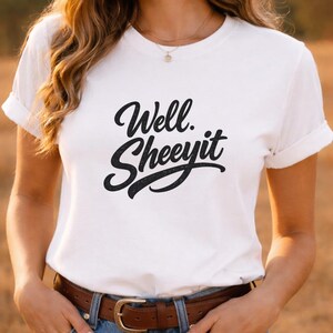 Könnte beinhalten: Weißes T-Shirt mit dem Schriftzug "Well. Sheeyit" in schwarzer, strukturierter Schrift. Das Shirt hat kurze Ärmel und einen Rundhalsausschnitt. Das Model trägt eine blaue Jeans und einen braunen Gürtel.