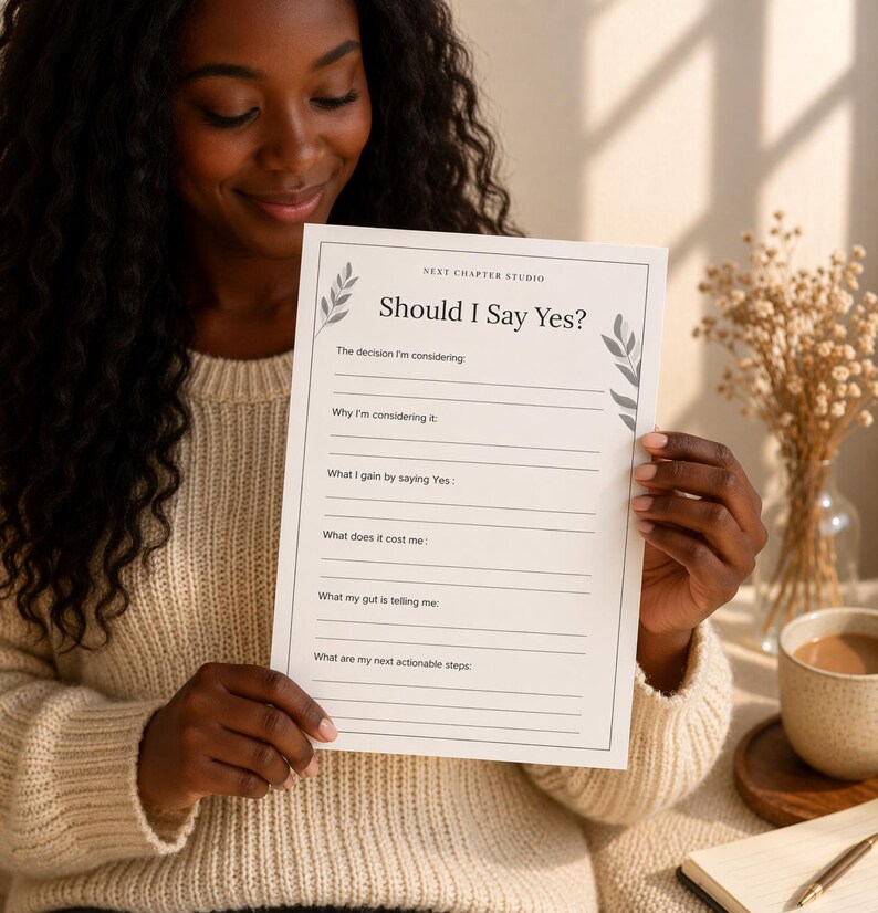 May include: A white paper with the text "Should I Say Yes?" and prompts for decision-making. The paper is held by a person wearing a cream-colored sweater. The paper has a floral design and the words "Next Chapter Studio".