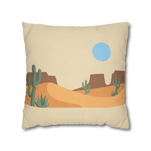 May include: A beige square pillow featuring a desert landscape design. The illustration includes tan sand dunes, brown rock formations, green cacti, and a blue sun. This decorative pillow adds a southwestern touch to any room.