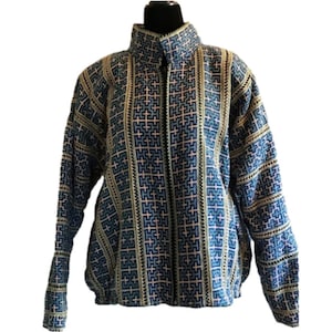 May include: A long-sleeved jacket featuring a high collar and a full-length front zip. The fabric displays a repeating geometric pattern in shades of blue, tan, and black, with vertical striped bands running along the front and sleeves.