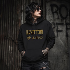 May include: Black hoodie with the gold text "LED ZEPPELIN" and four symbols below. The hoodie has a front pocket and a hood. The person in the image is wearing sunglasses and has tattoos on their arms.