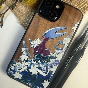 May include: A black iPhone case with a wood grain effect. The case features a colourful illustration of a character with a blue and white floral design. The case has a black border and camera cutout.