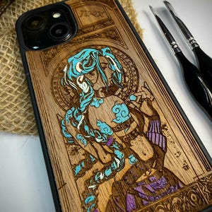 K&ouml;nnte beinhalten: Handy-H&uuml;lle aus Holz mit einer detaillierten Gravur eines Charakters mit blauen Haaren und Akzenten, mit dem Namen "JINX" oben eingraviert. Das Design befindet sich auf einem hellbraunen Holzmaserungshintergrund mit schwarzem Rand.