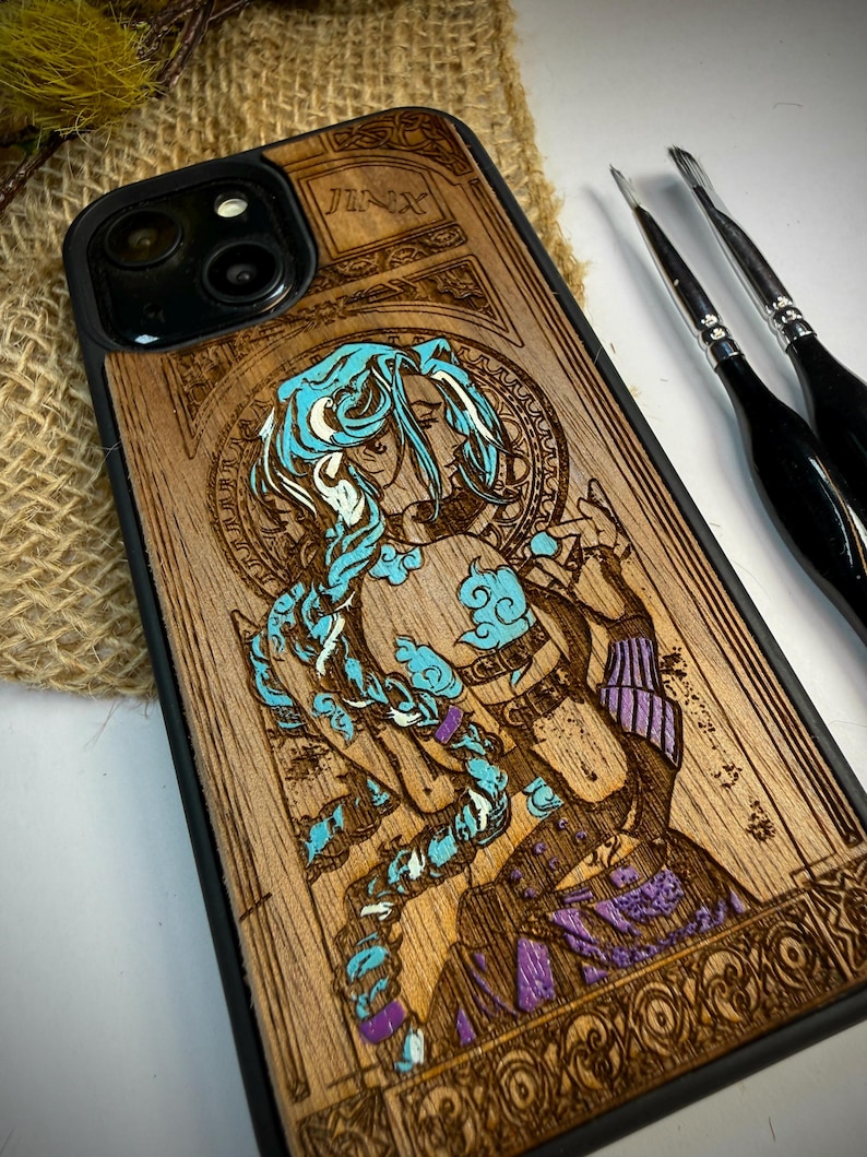 K&ouml;nnte beinhalten: Handy-H&uuml;lle aus Holz mit einer detaillierten Gravur eines Charakters mit blauen Haaren und Akzenten, mit dem Namen "JINX" oben eingraviert. Das Design befindet sich auf einem hellbraunen Holzmaserungshintergrund mit schwarzem Rand.