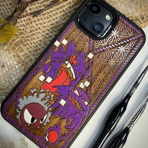 Pode incluir: Capa de telefone preta com parte traseira de madeira com um design esculpido de personagens de desenhos animados roxos e vermelhos. A capa tem uma borda preta e um padrão de grão de madeira detalhado. O design inclui um monstro roxo com a boca aberta.