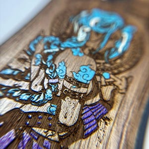 K&ouml;nnte beinhalten: Nahaufnahme einer Holzoberfl&auml;che mit einem detaillierten, lasergravierten Design. Das Kunstwerk zeigt eine Figur mit blauen Haaren und Akzenten, die ein dunkles Outfit mit lila und blauen Details tr&auml;gt. Die Holzmaserung ist sichtbar.