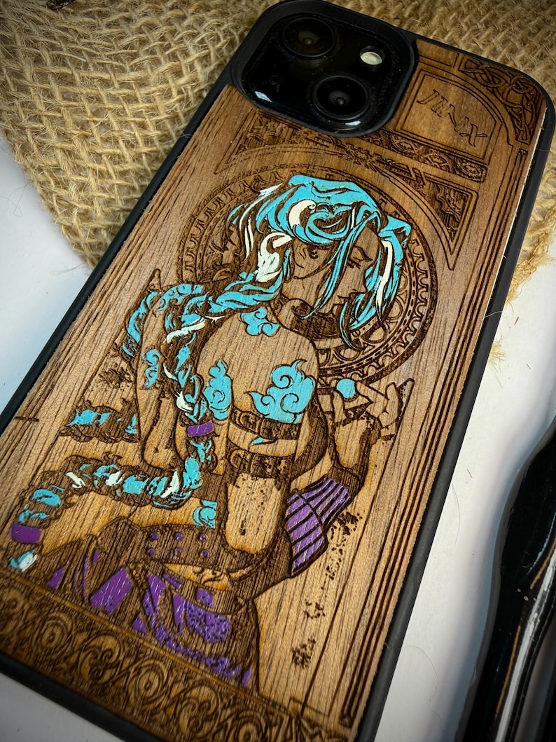 K&ouml;nnte beinhalten: Handy-H&uuml;lle aus Holz mit einem lasergravierten Design eines Charakters mit blauen Haaren und lila Akzenten. Das Wort "Jinx" ist oben sichtbar. Die H&uuml;lle hat einen schwarzen Rand und eine nat&uuml;rliche Holzmaserung.