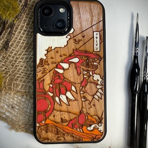 May include: Wooden phone case featuring a detailed, laser-etched design of a red and white creature with Japanese text. The case has a black border and a natural wood grain finish, showcasing the intricate artwork.