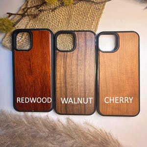 K&ouml;nnte beinhalten: Drei Handyh&uuml;llen aus Holz mit schwarzen R&auml;ndern. Die H&uuml;llen sind mit "Redwood", "Walnut" und "Cherry" beschriftet. Die Redwood-H&uuml;lle ist ein tiefes Rotbraun, die Walnussh&uuml;lle ist mittelbraun und die Kirschholz-H&uuml;lle ist hellbraun.