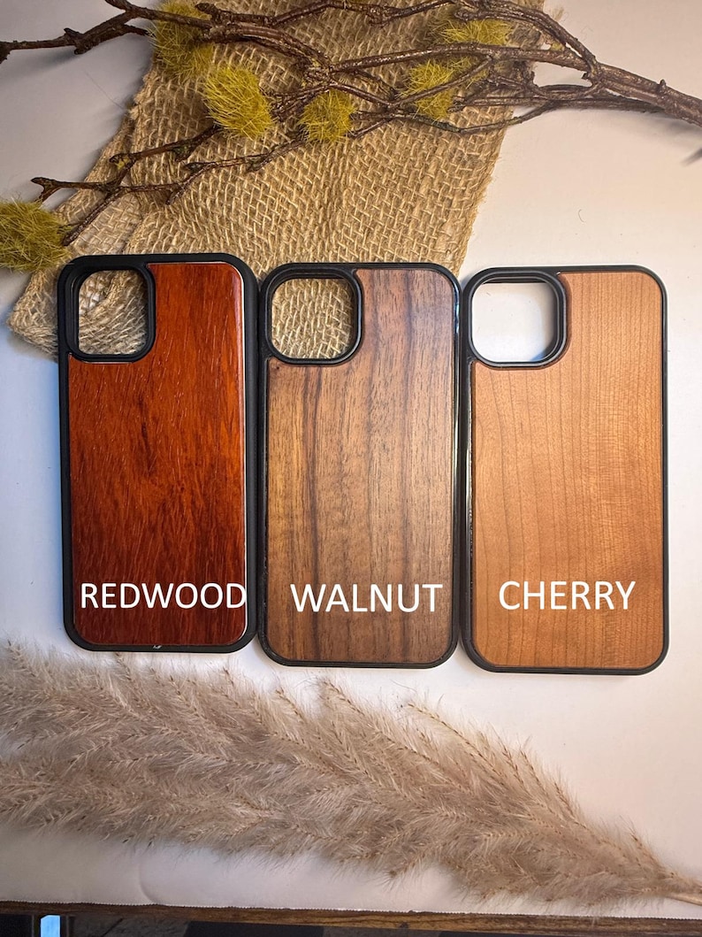 K&ouml;nnte beinhalten: Drei Handyh&uuml;llen aus Holz mit schwarzen R&auml;ndern. Die H&uuml;llen sind mit "Redwood", "Walnut" und "Cherry" beschriftet. Die Redwood-H&uuml;lle ist ein tiefes Rotbraun, die Walnussh&uuml;lle ist mittelbraun und die Kirschholz-H&uuml;lle ist hellbraun.
