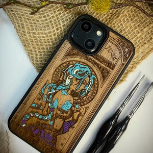 May include: Wooden phone case with a laser-etched design of a character with blue hair and accents. The case has a black border and the name "Jinx" is visible. The artwork is in shades of brown, blue, and purple.