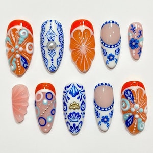 May include: A collection of ten artificial nails with various designs. The nails feature orange, white, blue, and pink colors. Designs include floral patterns, citrus fruit slices, and decorative embellishments. The nails are oval-shaped.