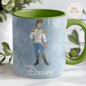 May include: A ceramic mug with a green handle and interior. The mug features a watercolor illustration of a prince in a white and gold uniform, with blue pants. The name "Derek" is printed on the mug.