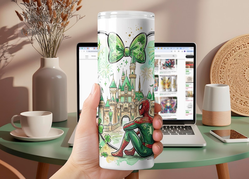 May include: A white tumbler featuring a green bow with shamrocks, a castle, and a seated Spider-Man in a green and red suit. The design includes fireworks and a green and white color scheme.