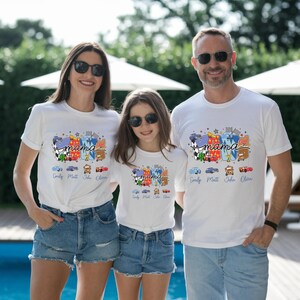 Puede incluir: Camisetas blancas con un estampado gr&aacute;fico colorido de coches de carreras de dibujos animados y la palabra mama en letra cursiva. Debajo del gr&aacute;fico hay cuatro peque&ntilde;as ilustraciones de coches con los nombres Emily, Matt, John y Olivia.