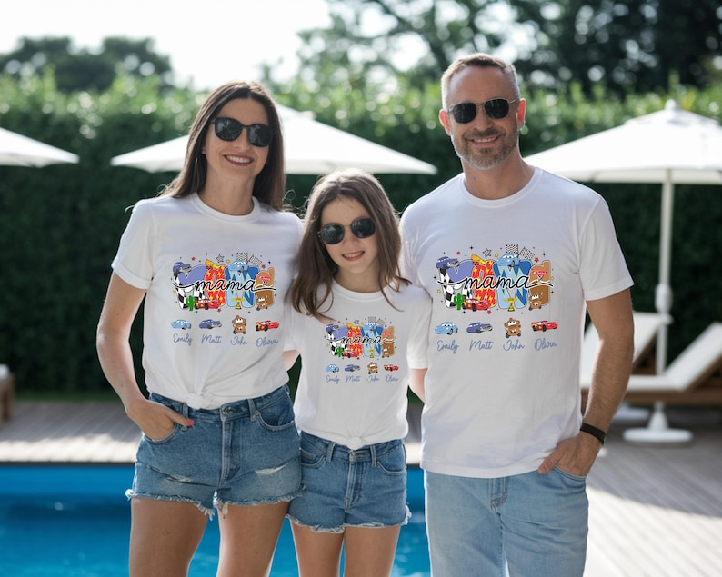 Puede incluir: Camisetas blancas con un estampado gr&aacute;fico colorido de coches de carreras de dibujos animados y la palabra mama en letra cursiva. Debajo del gr&aacute;fico hay cuatro peque&ntilde;as ilustraciones de coches con los nombres Emily, Matt, John y Olivia.