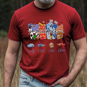 Puede incluir: Una camiseta roja de manga corta con un dise&ntilde;o gr&aacute;fico que muestra la palabra mama en cursiva sobre letras grandes que forman MOM. El dise&ntilde;o incluye varios personajes de coches de dibujos animados, banderas a cuadros y los nombres Emily, Matt, John y Olura.