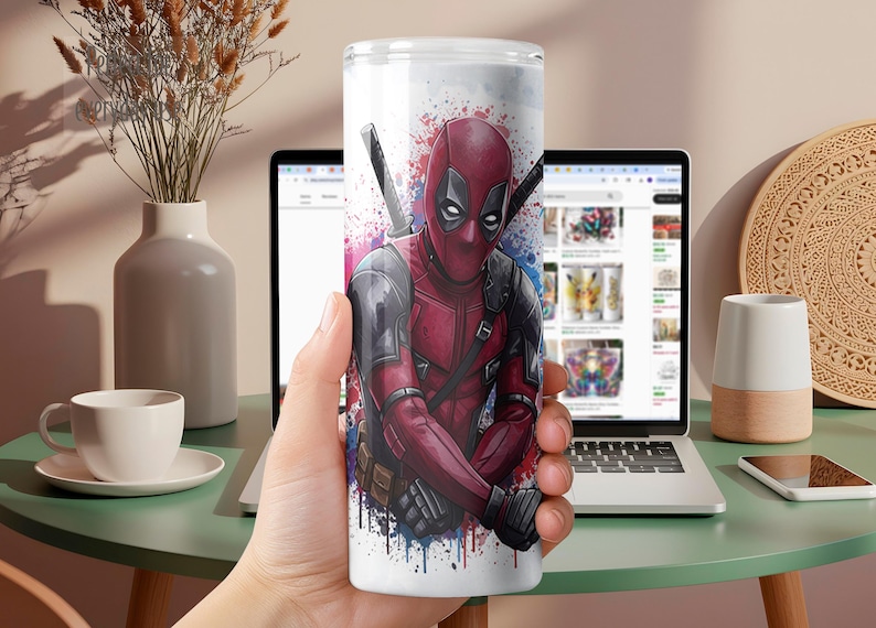 K&ouml;nnte beinhalten: Ein wei&szlig;er Becher mit einer lebendigen Illustration von Deadpool in seinem roten und schwarzen Anzug, komplett mit Schwertern. Das Design enth&auml;lt blaue und violette Farbspritzer, die eine dynamische &Auml;sthetik erzeugen. Ideal f&uuml;r Fans der Marvel-Figur.