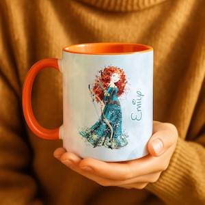 May include: White ceramic mug with an orange handle and interior. The mug features a watercolor illustration of a character with red hair, a bow, and a teal dress. The name "Emily" is written on the side.