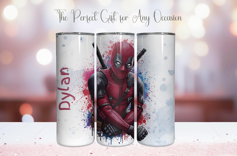 K&ouml;nnte beinhalten: Ein wei&szlig;er Becher mit einem Deadpool-Design in Rot und Schwarz. Der Becher hat einen Spritzer roter, blauer und violetter Farbe. Der Name "Dylan" ist auf der Seite aufgedruckt. Der Text "The Perfect Gift for Any Occasion" steht oben.