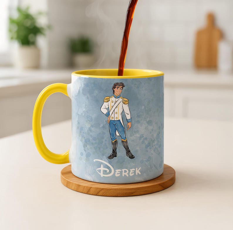 May include: A ceramic mug with a yellow handle and interior, featuring a cartoon illustration of a prince in a white and blue uniform. The mug has the name "DEREK" printed on it and sits on a wooden coaster. Coffee is being poured into the mug.
