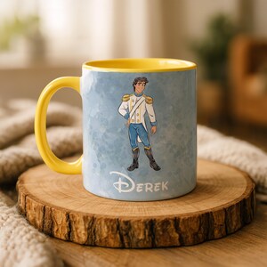 May include: A ceramic mug with a yellow handle and interior. The exterior features a cartoon illustration of a prince in a white and blue uniform against a light blue watercolor background. The name "Derek" is written in white.