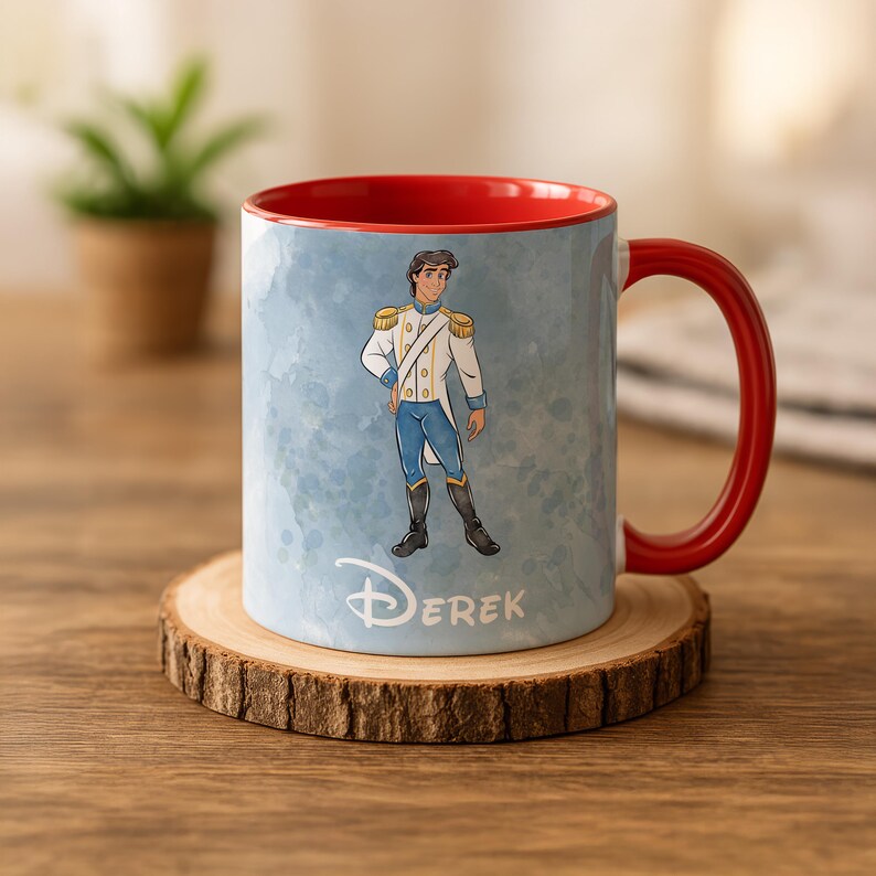 May include: A ceramic mug with a red interior and handle. The exterior features a watercolor-style illustration of a prince in a white and blue uniform. The name "Derek" is printed below the illustration. The mug sits on a wooden coaster.
