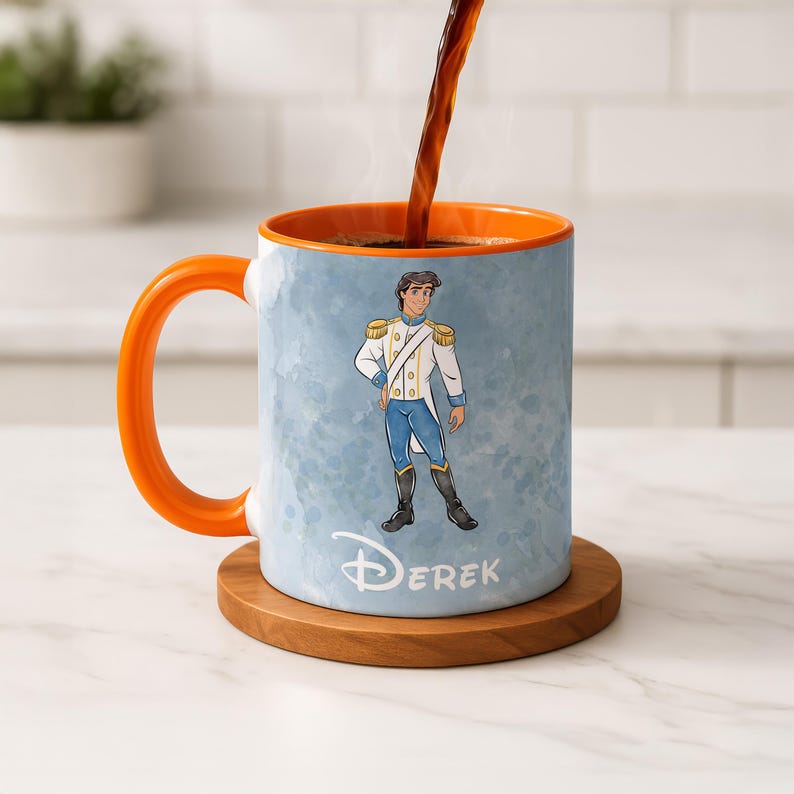May include: A ceramic mug with an orange handle and interior, featuring a cartoon illustration of a prince in a white and blue outfit. The mug has the name "Derek" printed on it, and is sitting on a wooden coaster. Coffee is being poured into the mug.