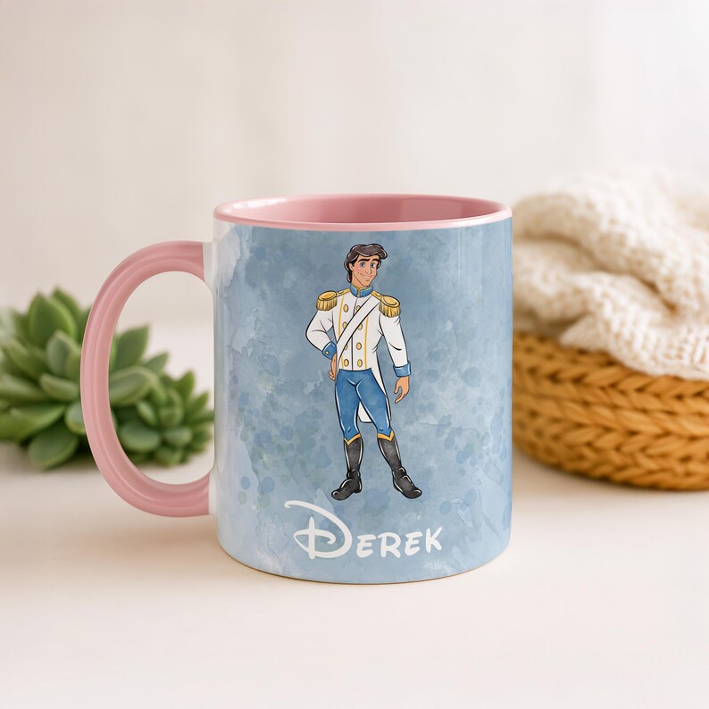 May include: A ceramic mug with a pink handle and interior. The mug features a watercolor-style illustration of a prince in a white and gold uniform with blue pants. The name "Derek" is written in a script font at the bottom.