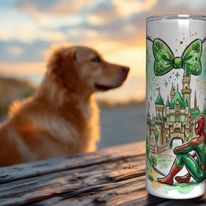 May include: A white tumbler featuring a green bow with shamrocks, a green castle, and a seated Spider-Man. The design has a St. Patrick's Day theme. A golden retriever dog is blurred in the background.