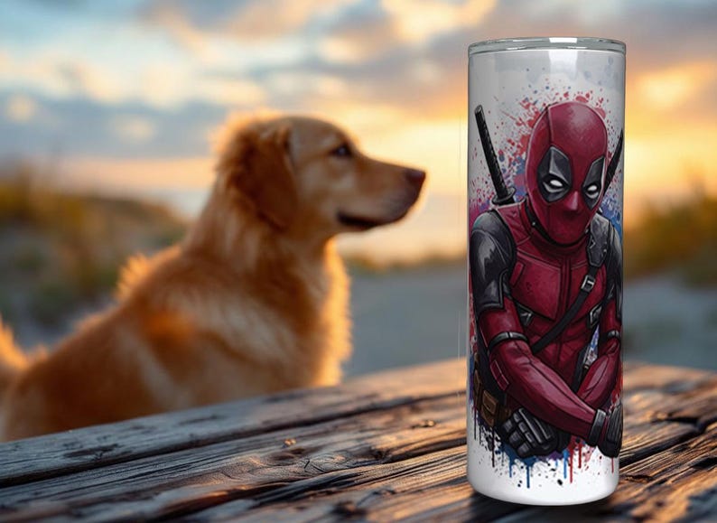 K&ouml;nnte beinhalten: Ein wei&szlig;er Becher mit einer lebendigen Illustration von Deadpool in seinem roten und schwarzen Anzug, mit zwei Katanas. Das Design umfasst farbenfrohe Farbspritzer. Ein Golden Retriever-Hund ist im Hintergrund unscharf.