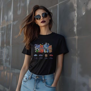 Puede incluir: Una camiseta negra de manga corta con un estampado gr&aacute;fico colorido de la palabra mama en una fuente estilizada. El dise&ntilde;o incluye cuatro coches peque&ntilde;os ilustrados debajo del texto, cada uno etiquetado con un nombre: Emily, Matt, John y Olive.