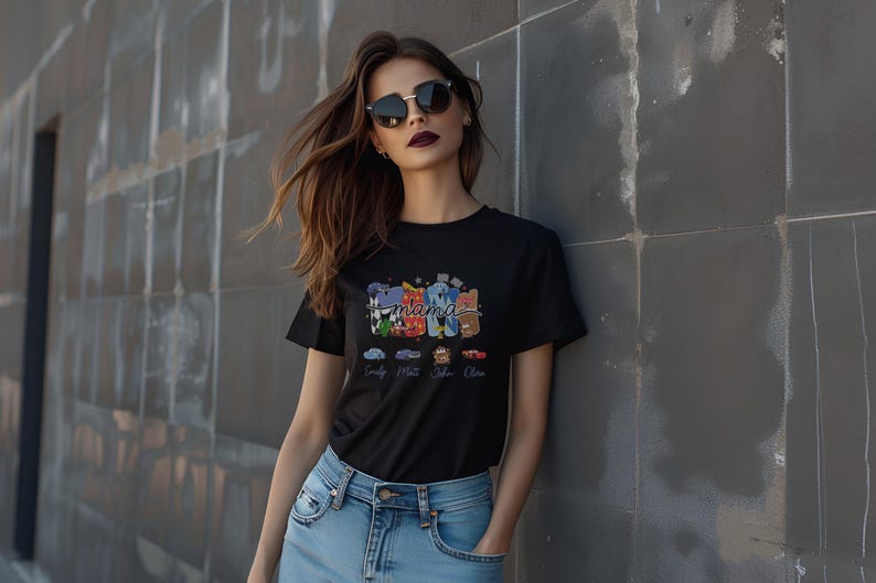 Puede incluir: Una camiseta negra de manga corta con un estampado gr&aacute;fico colorido de la palabra mama en una fuente estilizada. El dise&ntilde;o incluye cuatro coches peque&ntilde;os ilustrados debajo del texto, cada uno etiquetado con un nombre: Emily, Matt, John y Olive.