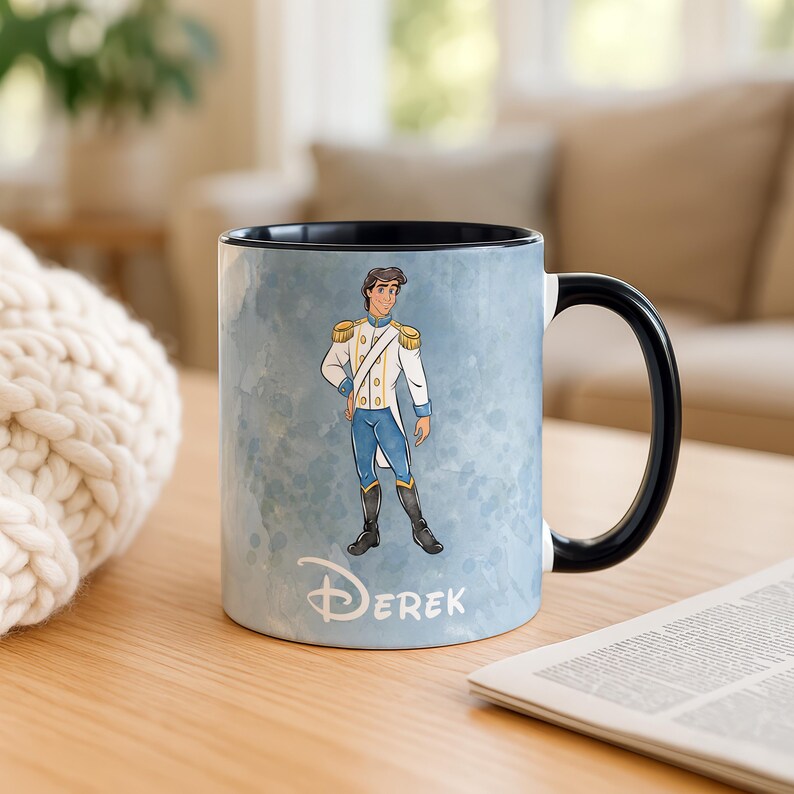 May include: A ceramic mug with a black handle and interior. The mug features a watercolor-style background with a cartoon illustration of a prince in a white and blue uniform. The name "Derek" is written in a script font below the illustration.