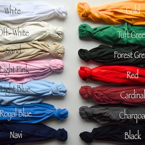 Puede incluir: Una colecci&oacute;n de catorce camisetas dispuestas en dos columnas, cada una atada en un nudo. Los colores incluyen blanco, blanco roto, arena, rosa claro, azul claro, azul real, azul marino, oro, verde c&eacute;sped, verde bosque, rojo, cardenal, carb&oacute;n y negro.