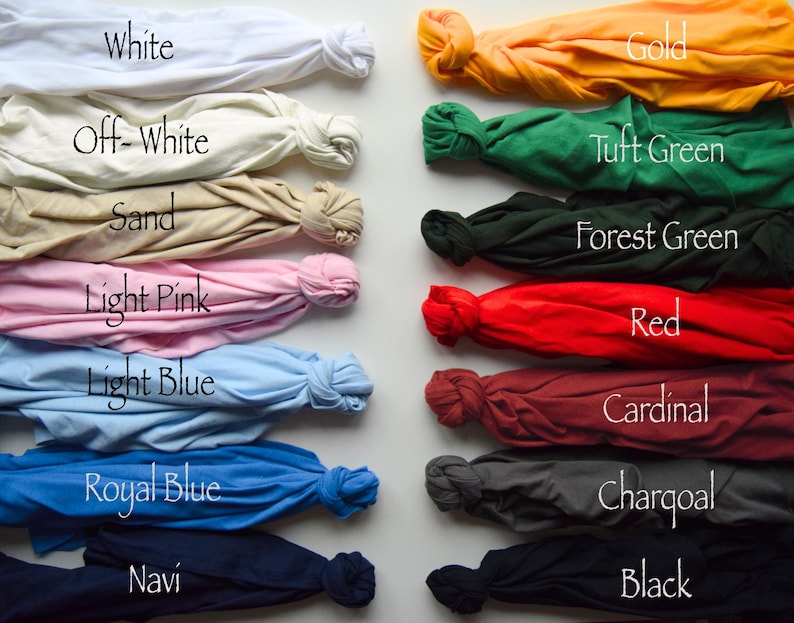 Puede incluir: Una colecci&oacute;n de catorce camisetas dispuestas en dos columnas, cada una atada en un nudo. Los colores incluyen blanco, blanco roto, arena, rosa claro, azul claro, azul real, azul marino, oro, verde c&eacute;sped, verde bosque, rojo, cardenal, carb&oacute;n y negro.