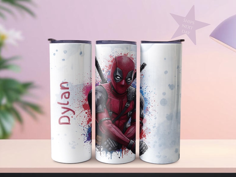 K&ouml;nnte beinhalten: Ein wei&szlig;er Becher mit einem Deadpool-Design. Der Becher hat einen schwarzen Deckel und einen Spritzer roter, blauer und violetter Farbe. Der Name "Dylan" ist vertikal in Rot auf der Seite aufgedruckt.