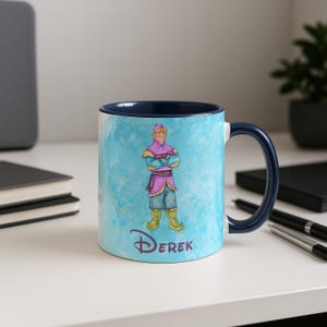Peut inclure: Mug en c&eacute;ramique avec int&eacute;rieur et anse bleus fonc&eacute;s. L'ext&eacute;rieur pr&eacute;sente une illustration de style aquarelle d'un personnage en tenue violette et bleue, avec le nom "Derek" en dessous. Le fond est un lavis bleu clair &agrave; l'aquarelle.