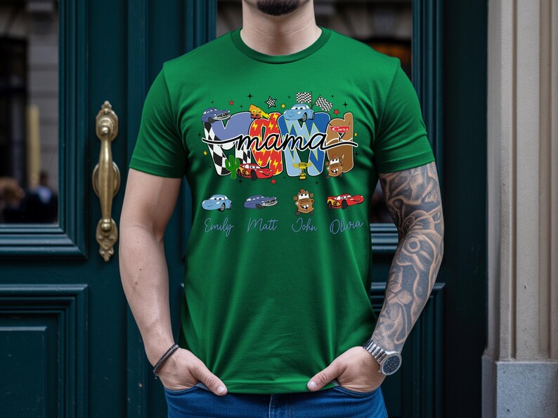 Puede incluir: Una camiseta verde con un estampado gr&aacute;fico que incluye la palabra mama en letra cursiva. El dise&ntilde;o presenta letras coloridas decoradas con varios personajes de coches de dibujos animados, banderas a cuadros y los nombres Emily, Matt, John y Olivia.