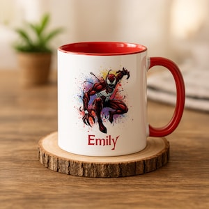 May include: White ceramic mug with a red interior and handle. The mug features a colorful graphic of a superhero character and the name "Emily" in red. The mug sits on a wooden coaster.