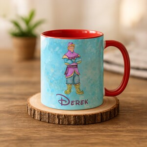 Peut inclure: Une tasse en c&eacute;ramique avec un int&eacute;rieur et une anse rouges. L'ext&eacute;rieur pr&eacute;sente une illustration de dessin anim&eacute; d'un personnage en tenue violette et bleue, avec le nom "Derek" en dessous. La tasse est pos&eacute;e sur un dessous de verre en bois.