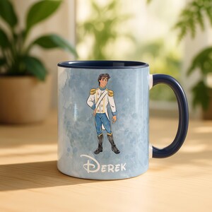 May include: A ceramic mug with a blue interior and handle. The exterior features a watercolor-style background and a cartoon illustration of a prince in a white and gold uniform. The name "Derek" is printed below the illustration.
