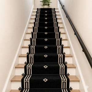 May include: A staircase with black carpet runners featuring a geometric design in cream. The runners are secured with black rods. The stairs have light wood treads and white risers. A black handrail runs along the right side of the stairs.