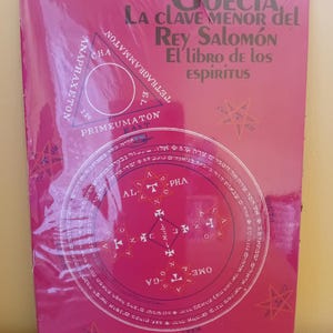 May include: A magenta-colored book titled "Goecia, La Clave Menor del Rey Salomón El libro de los espiritus" by Aleister Crowley. The cover features geometric shapes, text in multiple languages, and star illustrations.
