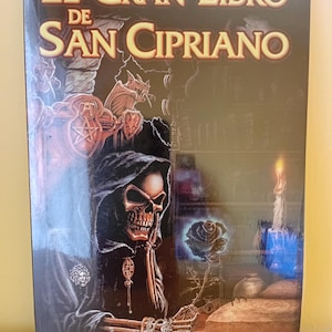 May include: A book titled "El Gran Libro de San Cipriano" with a dark, gothic illustration. The cover features a skeletal figure in a hooded robe, a glowing blue rose, and ornate jewelry. The background is a dark, detailed scene.