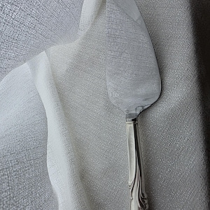 Può includere: Un coltello da torta argentato con un manico decorativo. Il coltello ha una lama larga e piatta e un manico dettagliato e ornato. Lo sfondo è un tessuto grigio chiaro.
