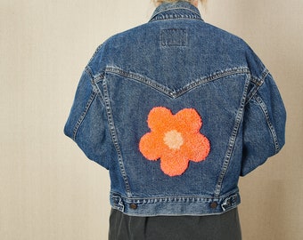 May include: A blue denim jacket with a large orange and pink flower patch on the back.