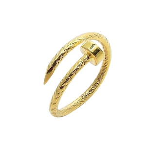 May include: A gold-coloured ring in the shape of a nail. The ring features a textured pattern on the band and a flat, round head. This nail ring is a distinctive piece of jewellery.