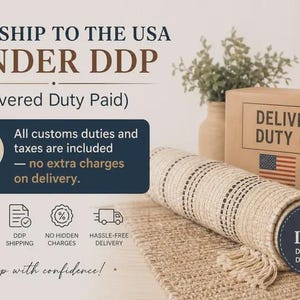 K&ouml;nnte beinhalten: Ein gerollter beiger Webteppich mit dunklen Streifen und Fransen, neben einem Karton mit der Aufschrift DELIVERED DUTY PAID USA und einer US-Flagge. Der Text enth&auml;lt WE SHIP TO THE USA UNDER DDP und All customs duties and taxes are included.