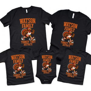 K&ouml;nnte beinhalten: Eine Kollektion aus f&uuml;nf schwarzen Kleidungsst&uuml;cken, bestehend aus vier kurz&auml;rmeligen T-Shirts und einem Baby-Body. Jedes zeigt eine orangefarbene Grafik eines laufenden Truthahns in Turnschuhen mit dem Text WATSON FAMILY TURKEY TROT AUSTIN, TX.